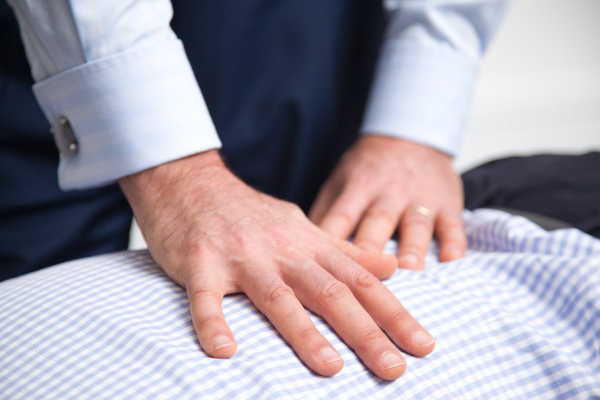 Dr Ari Diskin’s hands resting in contact along a client’s spine during a Nervous System Adjustment