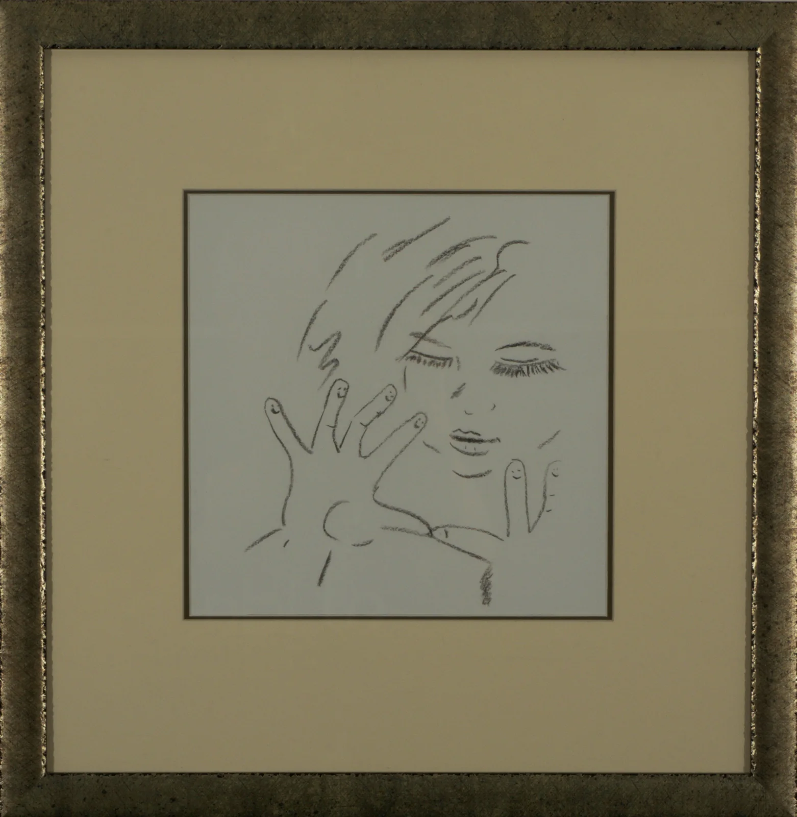 A framed charcoal drawing of a face and a pair of cradling hands, shown whole in its mount and gilt frame