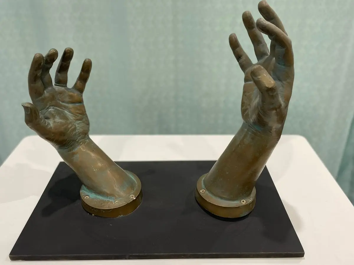 Cast-bronze sculpture of two cupped hands rising from a dark plinth