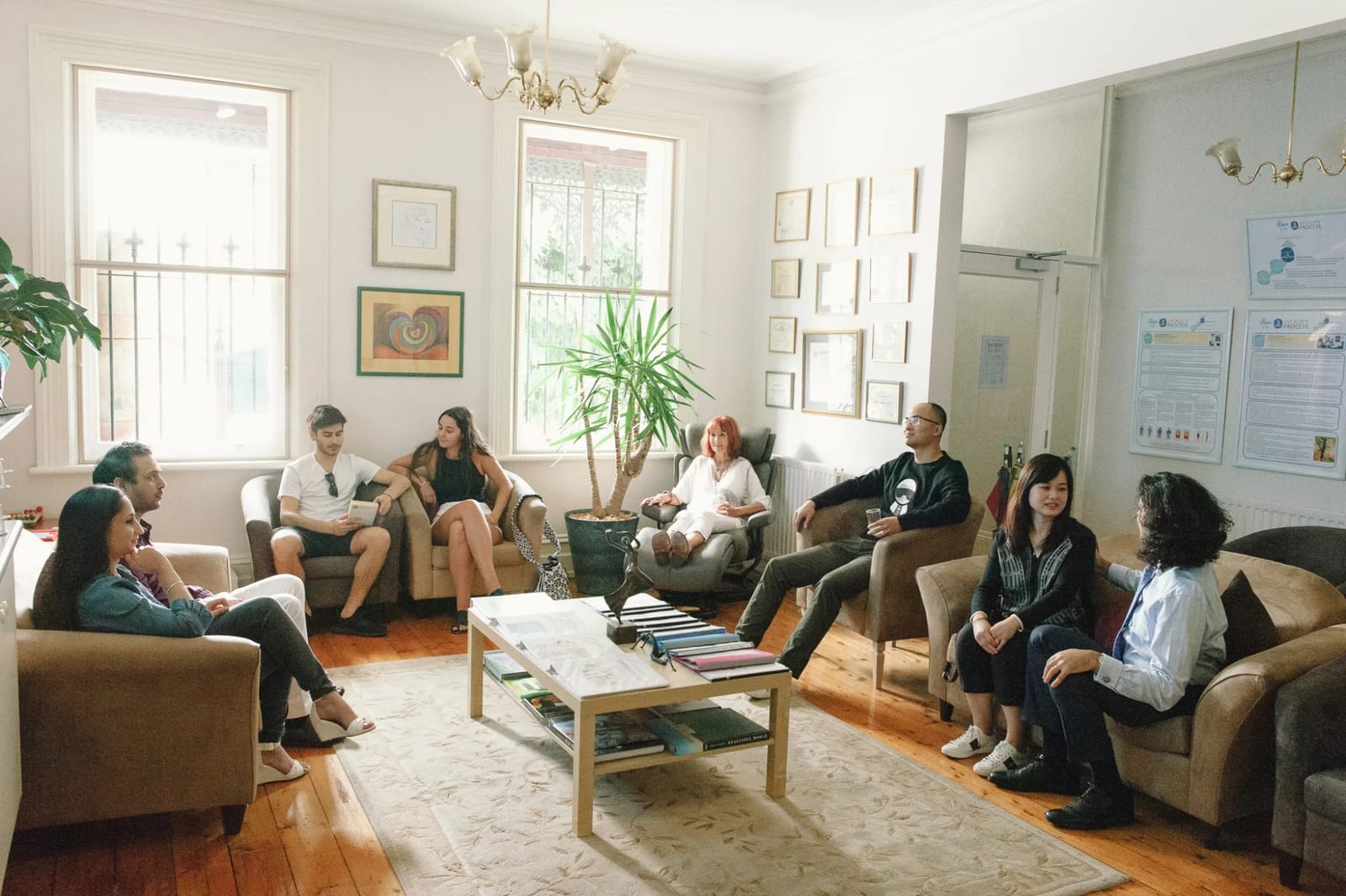 A group of people seated in armchairs around a low table, talking together in a Diskin Life lounge room with period windows and framed artwork on the walls.